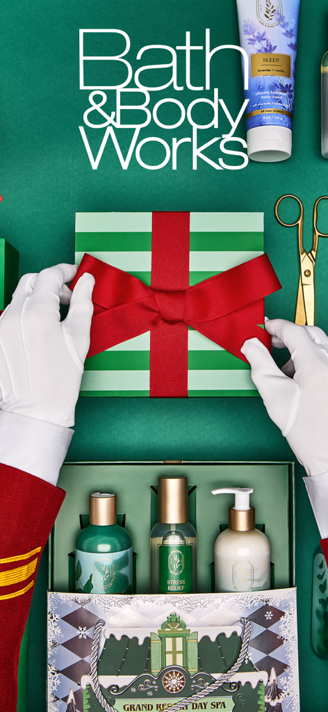 Manos con guantes blancos atando un lazo rojo en una caja de regalo de Bath and Body Works a rayas verdes y blancas