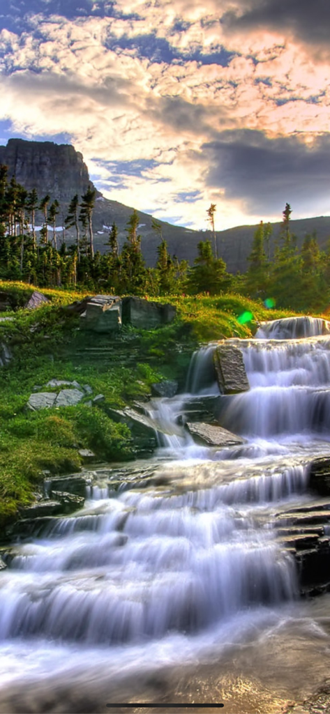 Kappboom - Cool Wallpapers - A stunning tiered waterfall cascading down a lush green mountain slope under a dramatic sky.