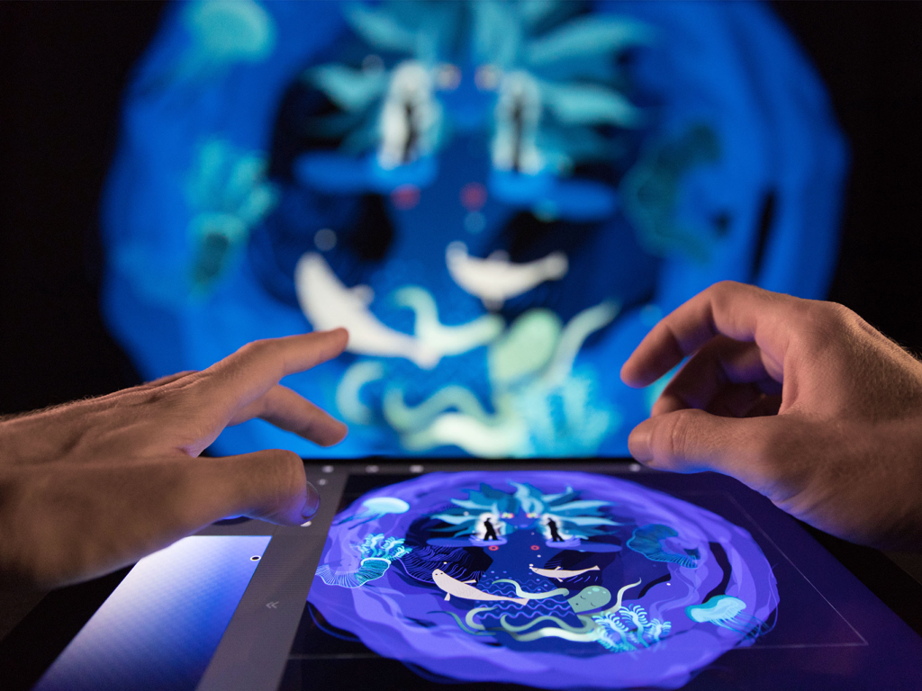 Una persona usando Tagtool SE en un iPad para crear arte digital que se proyecta simultáneamente en una pantalla grande