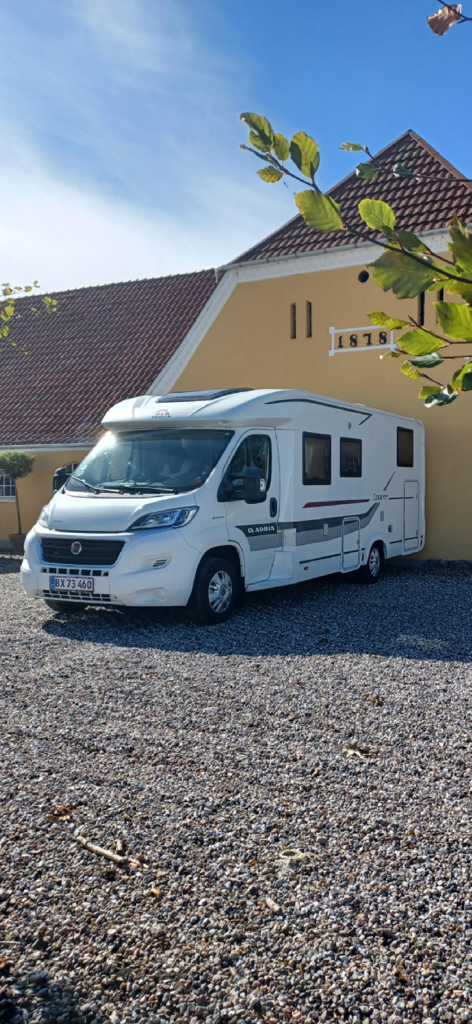 Pintrip - motorhome stopovers - White motorhome parked next to a historic yellow Danish farm building