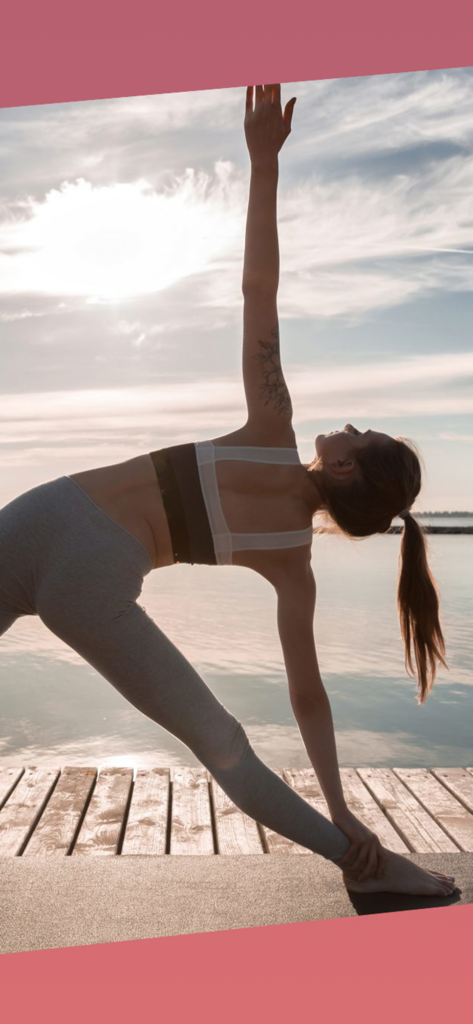 Woman practicing triangle yoga pose on a wooden deck by the sea