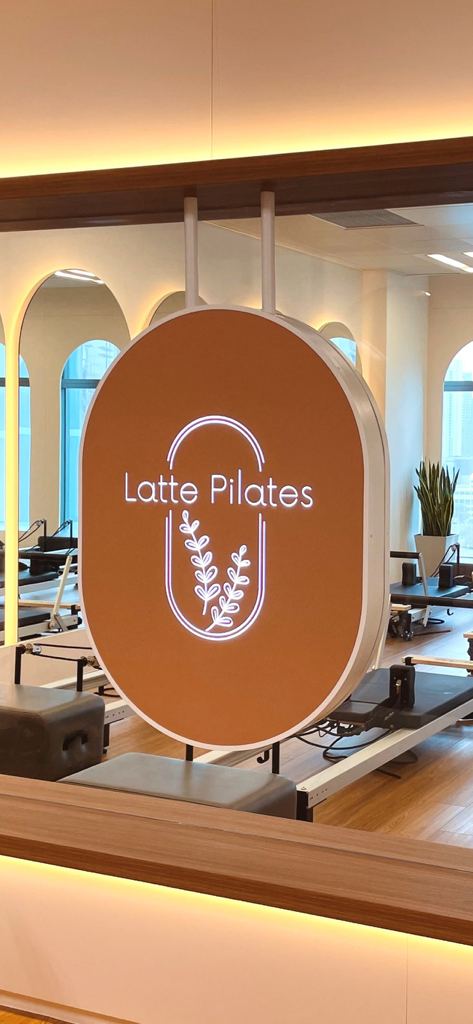 Latte Pilates HK - A neon sign displaying the Latte Pilates logo in a modern studio with pilates reformer machines.