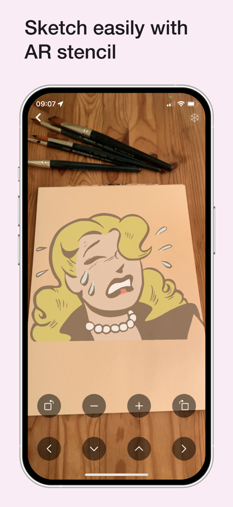Color Wheel - スマートフォン画面に、カラーホイールアプリのARステンシル機能が、物理的なスケッチパッド上に漫画の描画を投影している様子が表示されています。