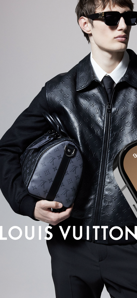 Modelo masculino usando um colete de couro com monograma Louis Vuitton e óculos de sol segurando uma mala de viagem