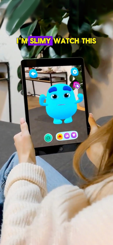 Talk to me Slimy: Brain Quiz - Una persona sosteniendo un iPad que muestra el personaje IA azul de Bicho en un entorno de sala de realidad aumentada.