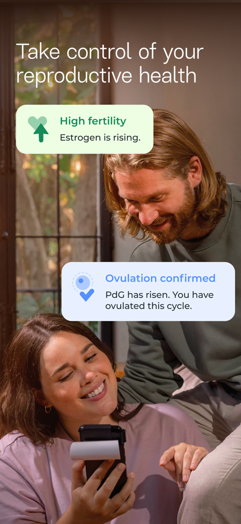 Una pareja sonriente mirando la app Inito en un smartphone que muestra la ovulación confirmada y el estado de alta fertilidad.