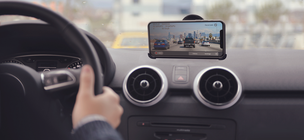 An iPhone mounted on a car dashboard using the Car Camera DVR PRO app to record driving footage on a highway