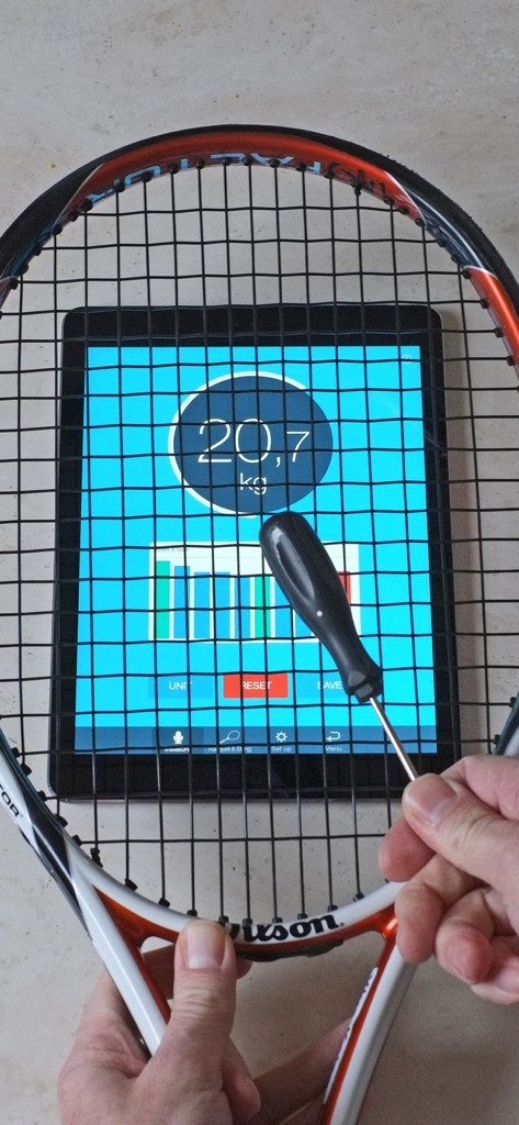 RacquetTune - String Tension - Una raqueta de tenis sostenida sobre una tableta que muestra los resultados de la medición de la tensión de las cuerdas en kilogramos