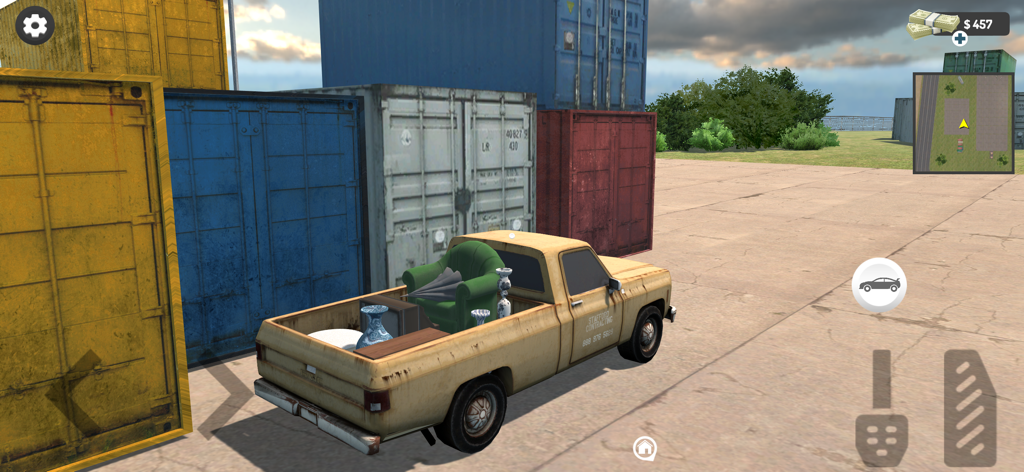 Auction Hunter Simulator : BId - Un pickup carico di mobili e oggetti parcheggiato accanto a container marittimi.
