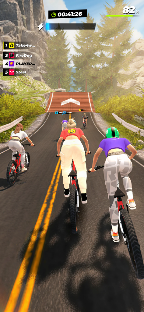 RUSH: Xtreme - Players racing mountain bikes through a forest road towards a wooden jump ramp in RUSH Xtreme.