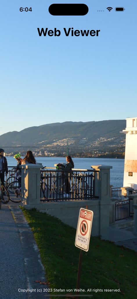 Webcam World Viewer - A scenic live webcam view of a waterfront with mountains and cyclists