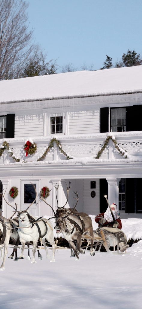 Santa Claus in his sleigh with reindeer in the front yard of a snowy house