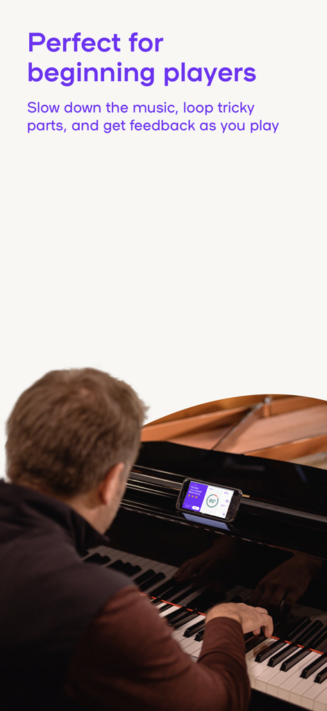 Playground: Real Piano Lessons - An adult learner using the Playground piano app on a smartphone to get real-time feedback while practicing on a grand piano