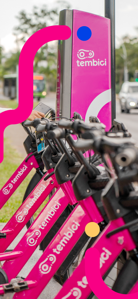tembici. - Filas de bicicletas compartidas Tembici de color rosa en una estación de anclaje de la ciudad con un usuario sosteniendo un smartphone para desbloquear un viaje.