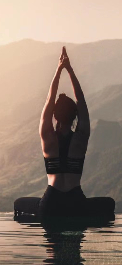 4S Fitness - A woman practicing yoga and meditating outdoors with a mountain background at sunset