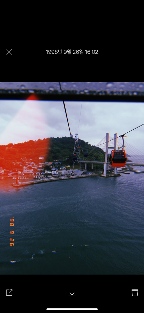 Foto estilo vintage tomada con Huji Cam con un teleférico sobre agua con un efecto de fuga de luz roja y un sello de fecha de 1998