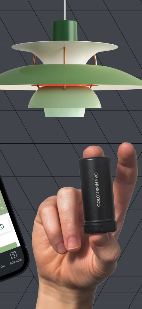 Mano sosteniendo un escáner de color digital Colourpin Pro cerca de una lámpara de diseñador verde.