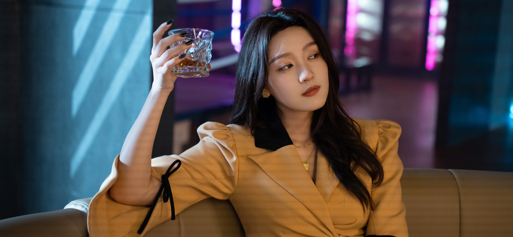 Una mujer hermosa con un blazer color canela sosteniendo un vaso de whisky en un bar cinematográfico de un juego de drama interactivo.