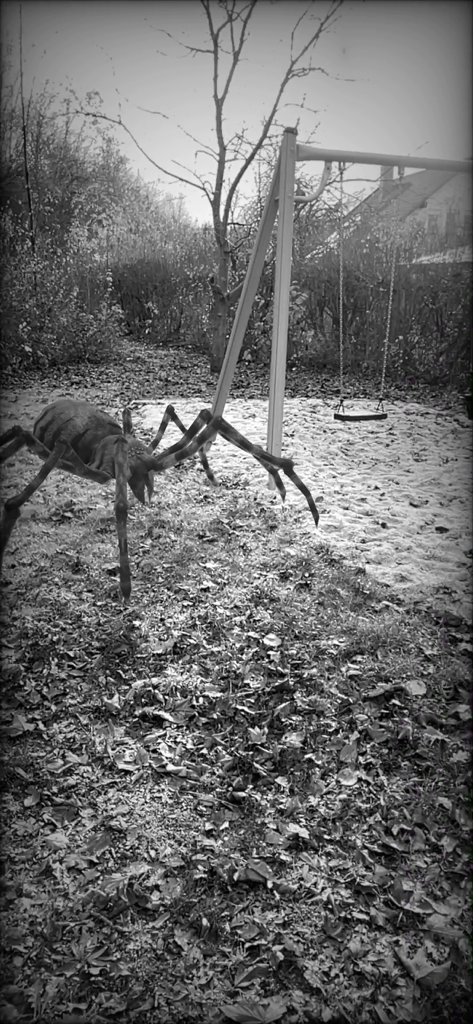 A giant augmented reality spider on a lawn next to a swing set with a black and white horror filter