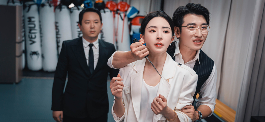 Una escena dramática de un juego de película interactiva con un hombre apuntando con un cuchillo al cuello de una mujer mientras otro hombre observa al fondo.