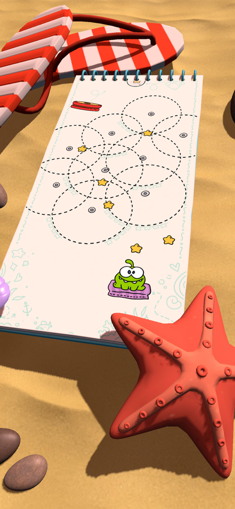 Cut the Rope Daily - Om Nom level design on a notebook resting on a sandy beach