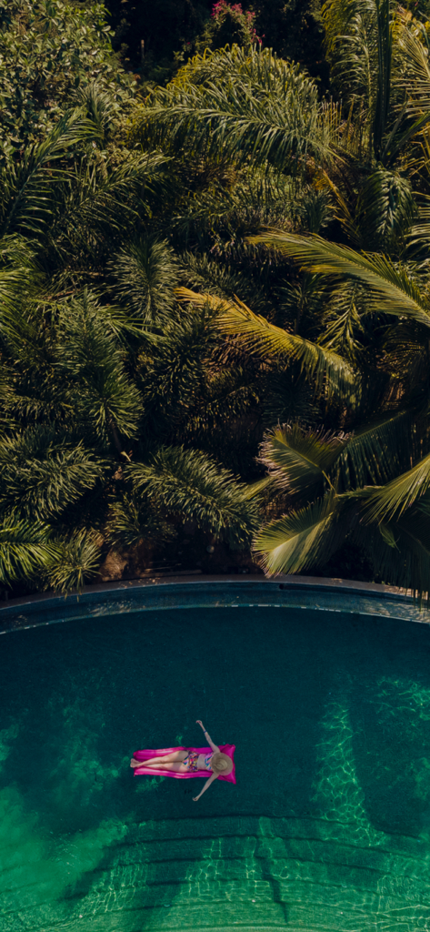 Marriott Experience - Aerial view of a person relaxing on a pink float in a tropical resort pool