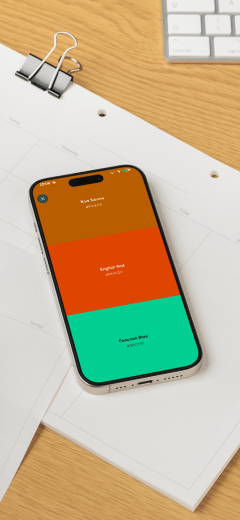 Un smartphone que muestra una paleta de tres colores con Sienna Tostada, Rojo Inglés y Azul Pavo Real en la aplicación Diccionario de Colores de Wada.