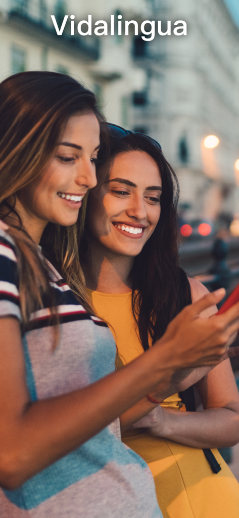 Two young women smiling while using the Vidalingua French dictionary app on a smartphone outdoors