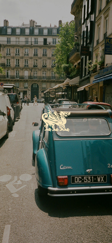 Un'auto d'epoca Citroen color petrolio parcheggiata in una strada parigina con sovrapposto un logo dorato a forma di drago.