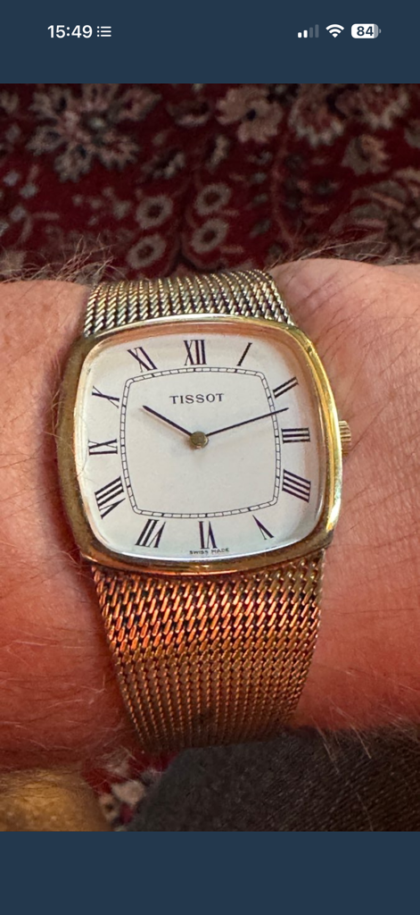 CollectAll Collections - Close-up de um relógio Tissot antigo dourado com algarismos romanos e uma pulseira de malha.