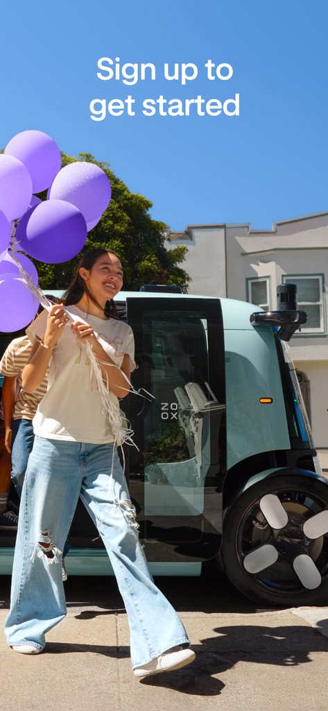 Zoox - A happy woman holding purple balloons walks past a light blue Zoox robotaxi on an urban street.