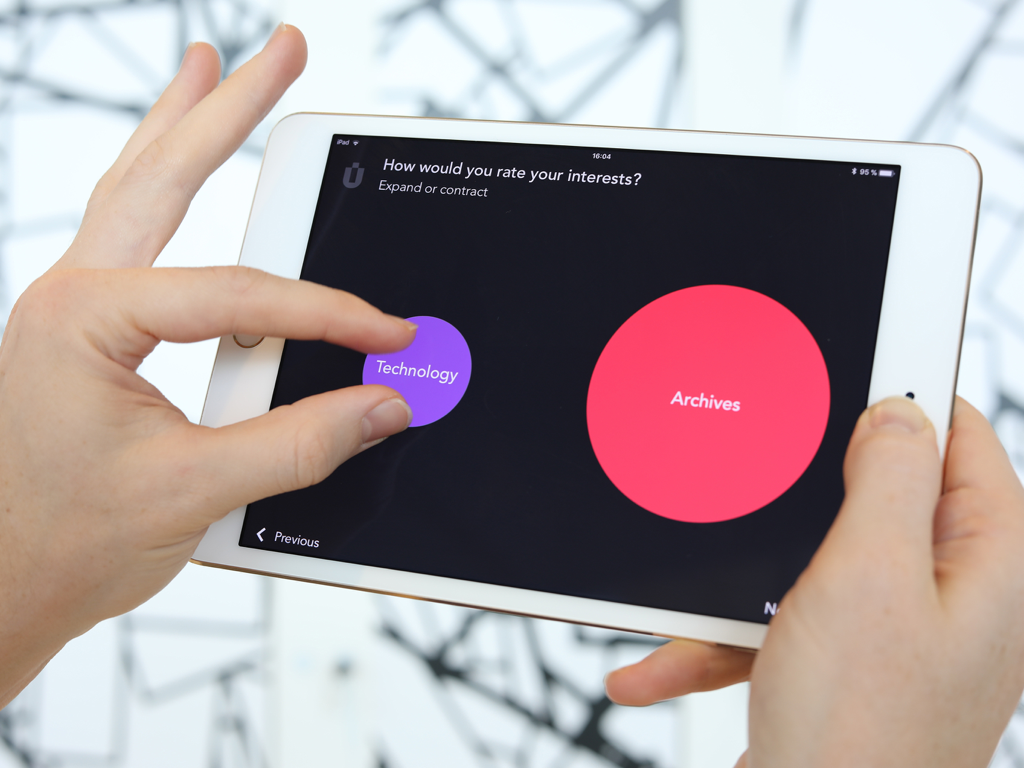 A person using a tablet to interactively rate their interests in a museum exhibit by resizing colored circles on the screen.