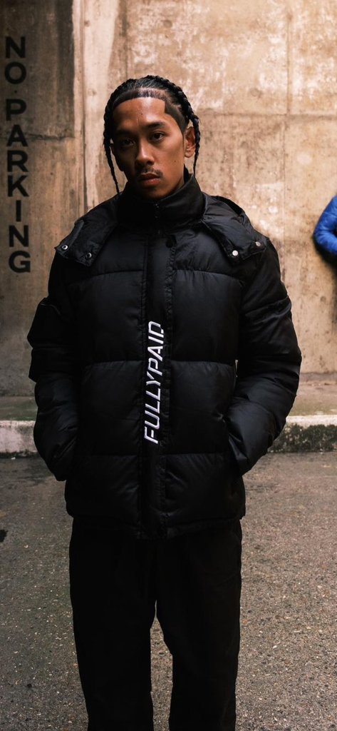 FULLYPAID CLOTHING - A man wearing a black FULLYPAID branded puffer jacket in an urban street setting