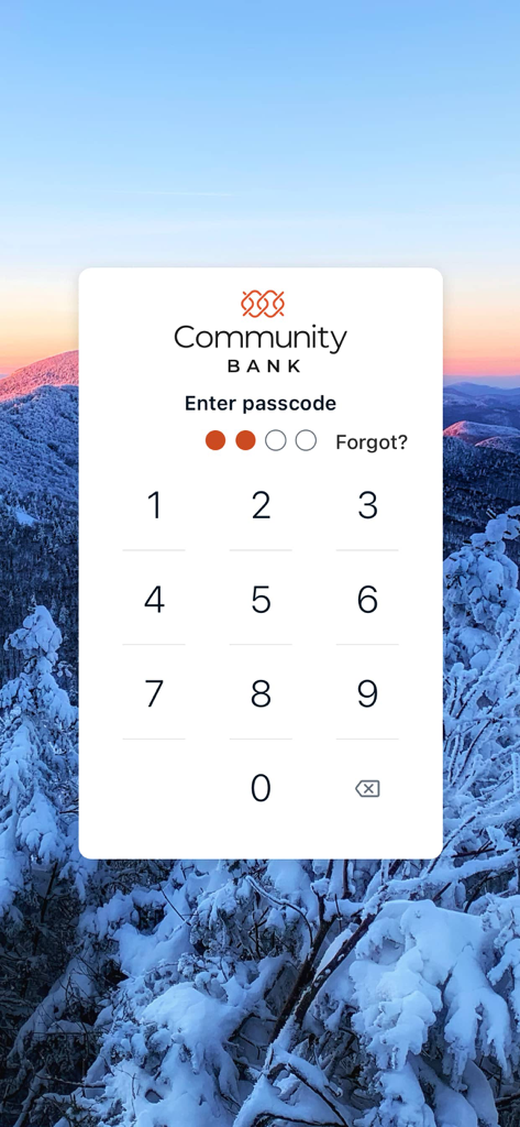 Pantalla de inicio de sesión de CBNA Mobile Banking que muestra un teclado numérico para la entrada del código de acceso sobre un fondo de paisaje de montaña nevada.