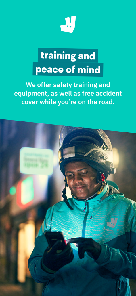 Deliveroo rider wearing a helmet and jacket checking his phone at night.