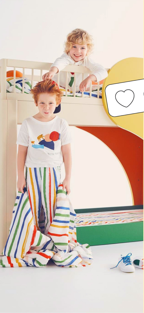 Zwei Kinder, die in einem farbenfroh gestalteten Kinderzimmer mit bunter Bettwäsche und modernen Möbeln spielen.