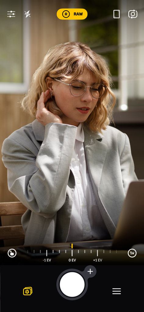A woman with glasses captured using the Camera Plus app interface with RAW mode and manual exposure controls