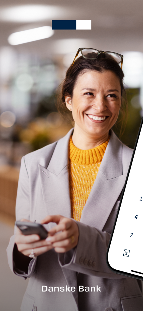 Une femme professionnelle souriante utilisant un smartphone avec l'interface de l'application District Mobile de Danske Bank affichant la connexion biométrique.