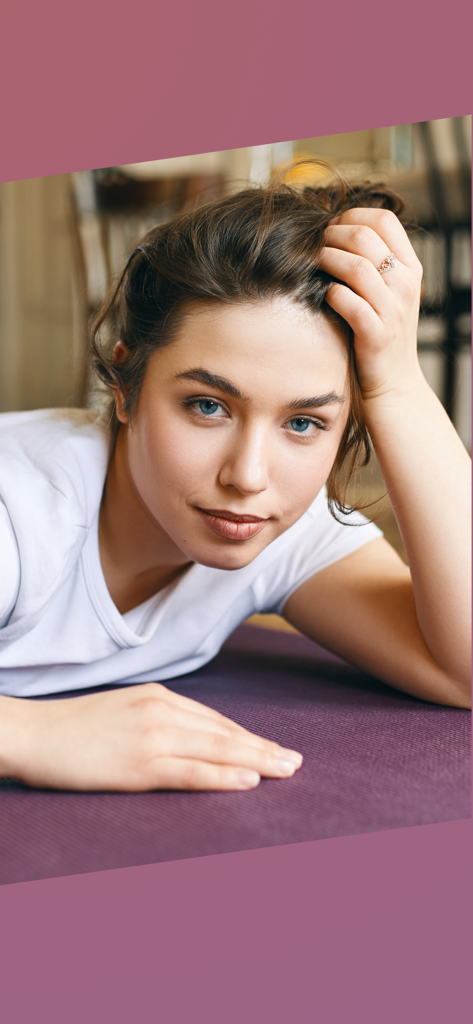 Lazy Workouts - A young woman lying comfortably on a purple yoga mat looking at the camera.