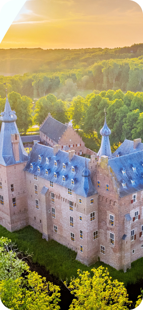 Castle.Tips-beautiful Castles! - A historic brick castle with blue-gray turrets surrounded by a lush green forest at sunset