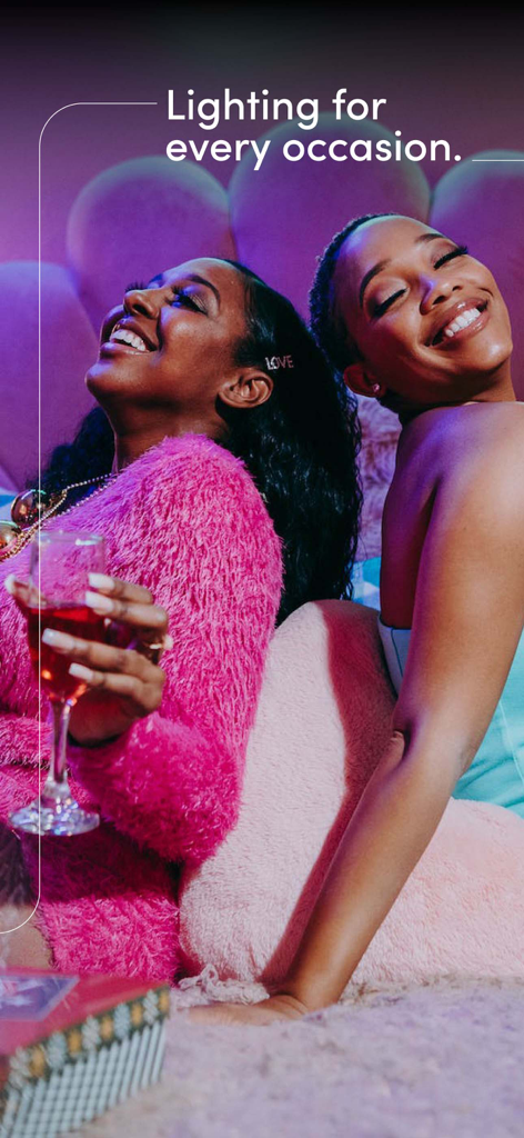 Dos mujeres riendo y disfrutando de una reunión social con iluminación inteligente vibrante en rosa y azul.