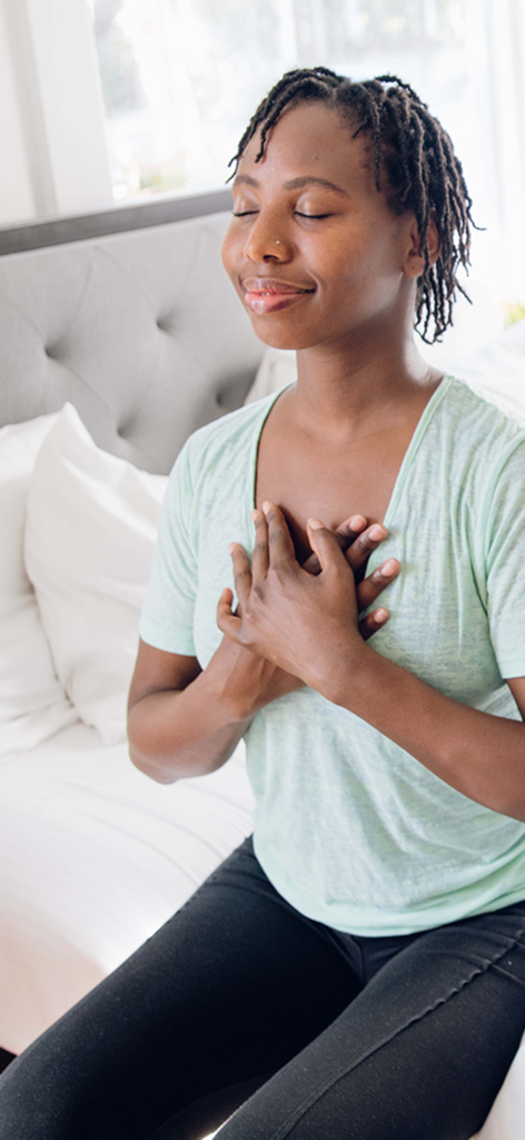 Yoga Wake Up: Alarm & Stretch - A peaceful woman sitting on her bed with eyes closed and hands over her heart practicing a morning meditation routine