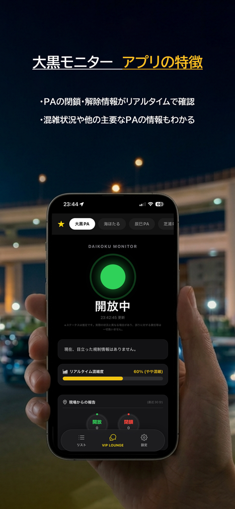 Uma mão segurando um smartphone exibindo o aplicativo PA-monitor mostrando um status Verde Aberto para a Área de Estacionamento Daikoku à noite