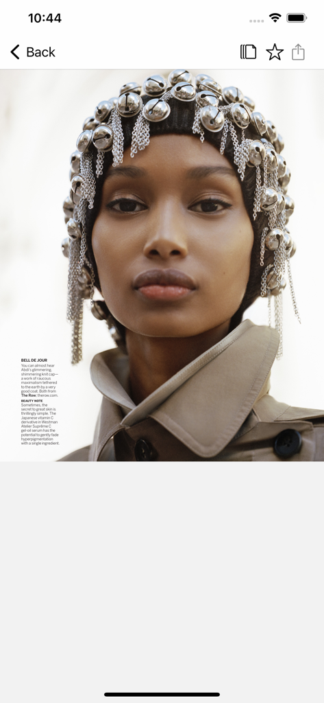 Mannequin de haute couture portant un couvre-chef en forme de cloche argenté et un trench-coat dans l'application Vogue.