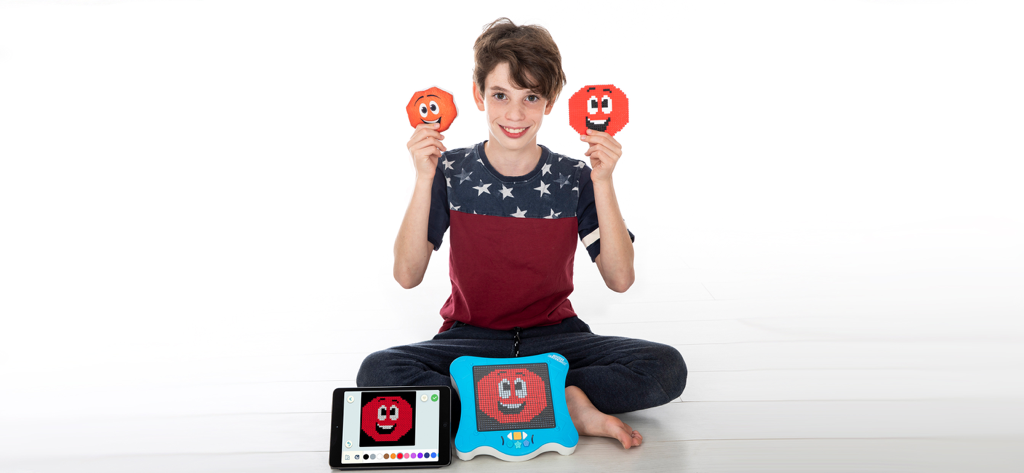 A young boy showing pixel art crafts next to a smART pixelator device and its companion app on a tablet.