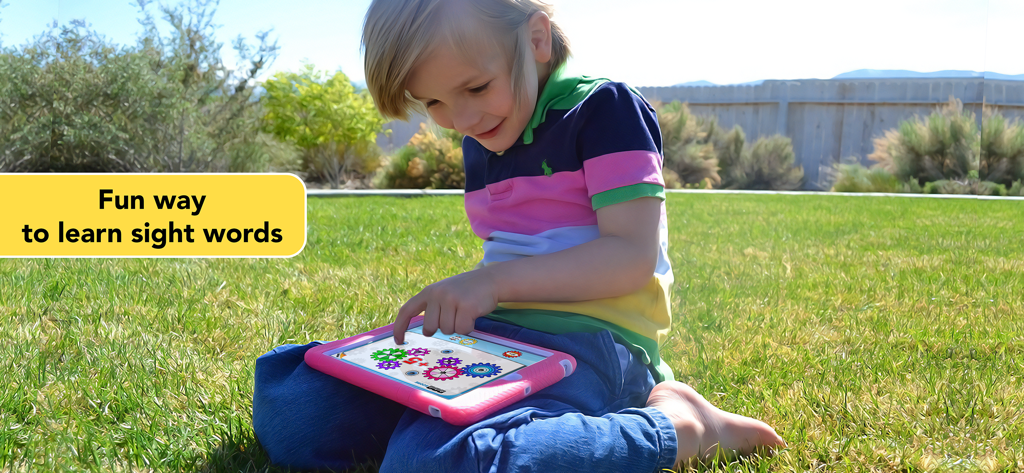 Sight Words Reading Games ABC - Un bambino piccolo che gioca a un gioco educativo di lettura di parole Dolch su un tablet seduto sull'erba all'aperto.