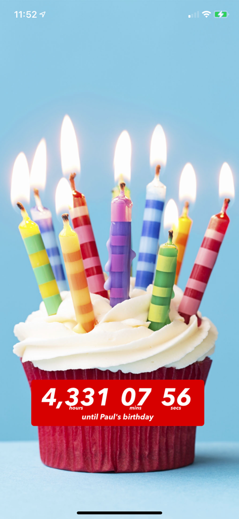 A red birthday cupcake with lit candles and a digital countdown timer until Paul's birthday.