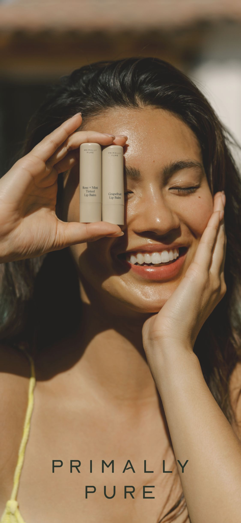 Primally Pure - Uma mulher sorrindo segurando dois protetores labiais Primally Pure sobre os olhos