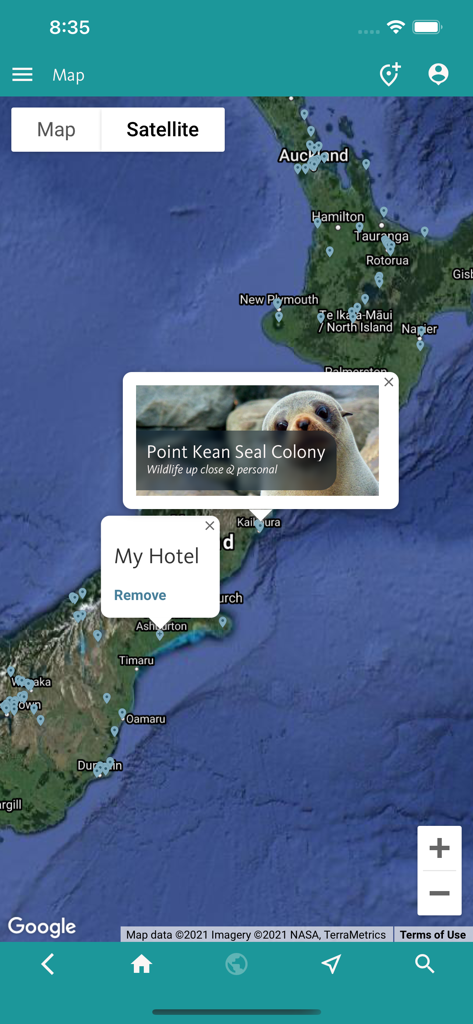 Mapa satelital de Nueva Zelanda en la aplicación que muestra marcadores de viaje para una colonia de focas y un pin de hotel personal.