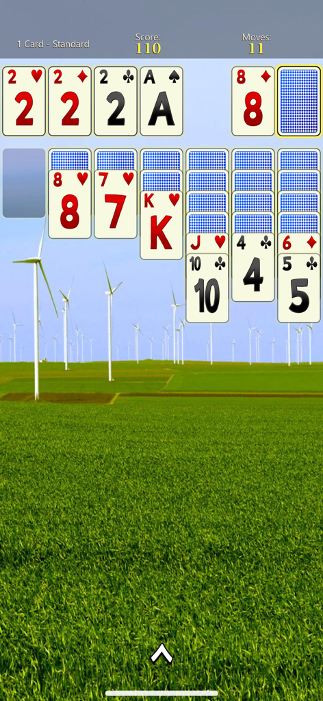 Solitaire Mobile - Solitaire Mobile gameplay screen showing big cards for easy visibility over a scenic landscape background with wind turbines.